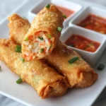 Crispy crab rangoon egg rolls stacked on a plate, showing golden brown wrappers and creamy crab filling